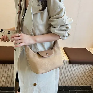 Detail of khaki suede crescent hobo bag with leather flap and strap on beige trench coat