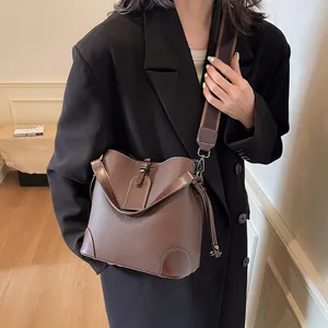 Détail d'un sac seau en cuir marron avec coins renforcés et large bandoulière en tissu