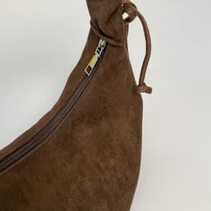 Close-up of brown suede shoulder bag featuring smooth zipper and decorative knot detail