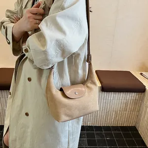 Model wearing a beige suede half-moon hobo bag with a silver metal buckle in a room