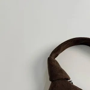 Detail of dark brown suede shoulder bag showing knotted strap and smooth zipper texture