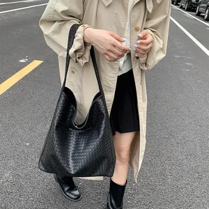 Street style view of a black woven leather tote bag paired with a classic khaki trench coat