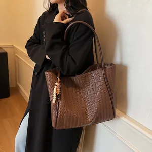 Close-up of brown woven tote bag with bead charms on a model in a black coat