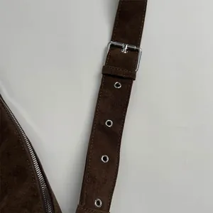 Detail of adjustable strap with silver buckle and eyelets on brown matte crossbody bag