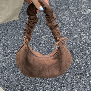 Close-up of brown pleated handle bag with decorative bow ties and suede texture