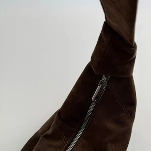Detail of dark brown suede crossbody bag showing silver zipper and knotted strap design