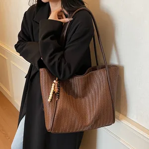 Detail of dark brown woven tote bag with ethnic bead tassel charm and long shoulder strap