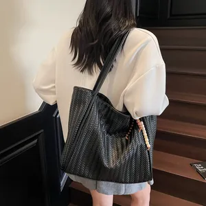 Detail view of large black woven tote bag with beaded charm and shoulder strap for commute