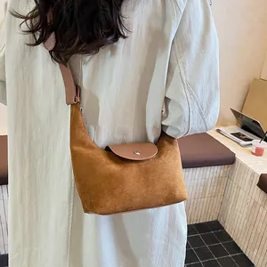 Detail view of brown suede dumpling bag with leather flap and metallic snap closure