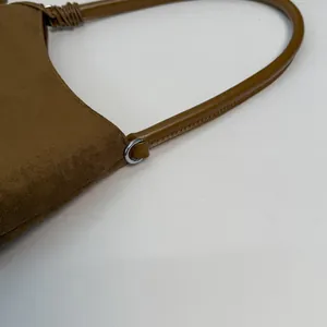 Macro detail of dark brown suede shoulder bag showing metal ring and smooth leather strap