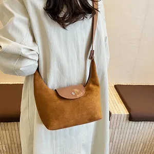 Detail of warm brown suede crossbody half-moon bag with leather flap and metal buckle