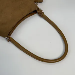 Detail of caramel suede bag with leather handle and decorative knot accents