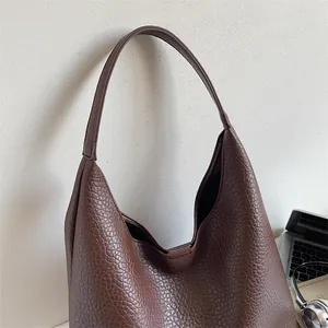 Macro detail of deep brown lychee grain leather on a large retro hobo shoulder bag