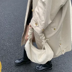 Detail of beige pleated dumpling bag with drawstring knots on a khaki trench coat