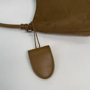 Close-up of brown suede shoulder bag featuring a smooth leather tag and silver metal ring