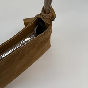 Detail of dark brown suede shoulder bag featuring a silver zipper and knotted leather strap