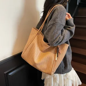Brown woven texture tote bag with wooden bead pendant shown on a model on stairs