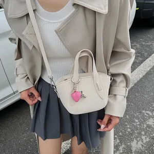 Dettaglio mini borsa crema con ciondolo a cuore rosa e portachiavi in metallo argento