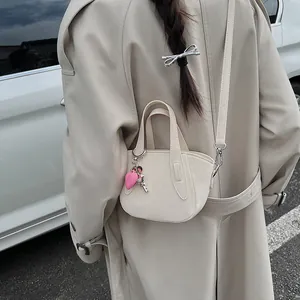 Dettaglio mini borsa crema con ciondolo a cuore rosa e charm chiave argento