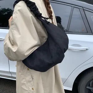 Detail of black drawstring hobo bag with pleated strap worn with a khaki trench coat