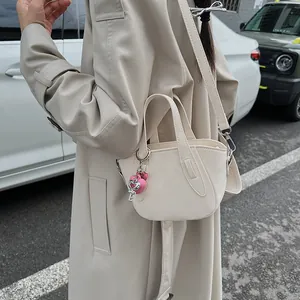 Elegante borsa a mano in pelle crema con ciondolo a cuore rosa su sfondo urbano