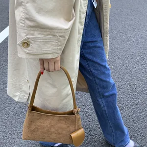 Detailed texture of brown suede shoulder bag with smooth leather trim on khaki trench coat