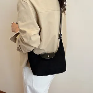 Detail of black suede shoulder bag with leather flap and silver snap button on a model