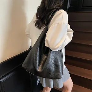 Close-up of black lychee grain leather tote bag worn by a model in a minimalist setting