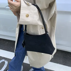 Detail of black suede trapezoid underarm bag with sleek leather strap in street setting