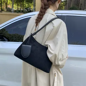 Detail of black suede shoulder bag with smooth leather pocket on female model outdoors