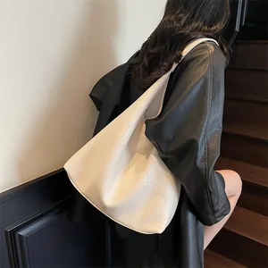 Close-up of white pebble grain tote bag worn over the shoulder against a dark jacket