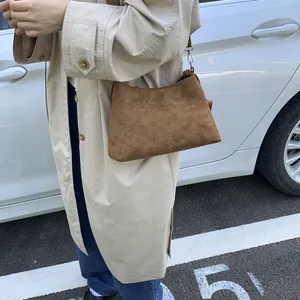 Brown suede crossbody bag shown on a model wearing a beige coat in a street setting