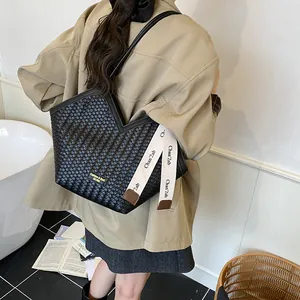 Détail d'un sac cabas tissé noir avec ouverture en V et ruban à lettres blanc décoratif
