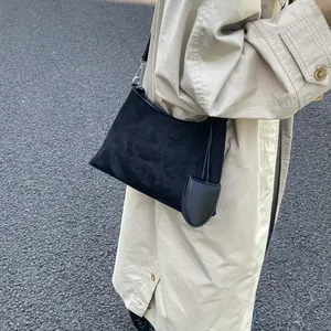 Detail of black matte shoulder bag with a small semi-circle charm on a trench coat