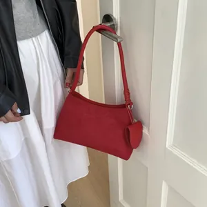 Close-up of red suede underarm bag with heart pendant hanging on white door handle