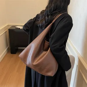 Detail of a large brown leather tote bag with lychee grain texture shown from the side