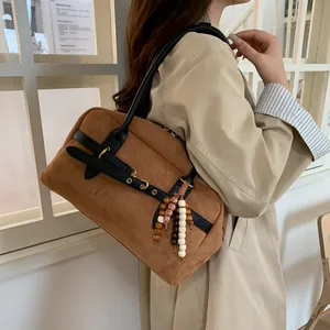 Close-up of brown suede handbag with black leather trim and colorful wooden bead tassel