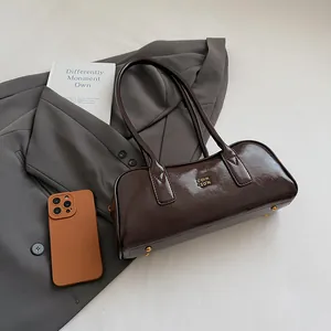 Detailansicht der dunkelbraunen Lackleder-Boston-Bag mit Goldlogo und schützenden Metallfüßen