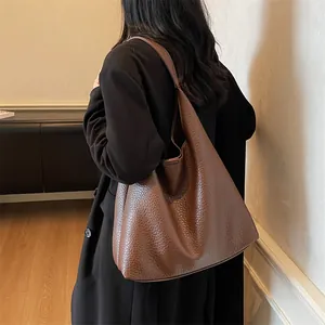Brown leather tote bag worn by a model in a dark coat, showing its large capacity and texture