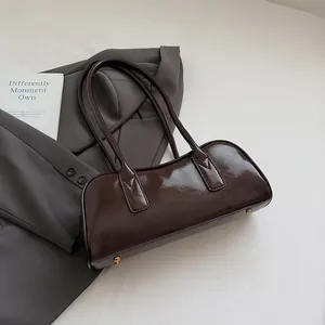 Detail der dunkelbraunen Glanz-Boston-Tasche mit goldenen Bodenfüßen auf grauem Blazer