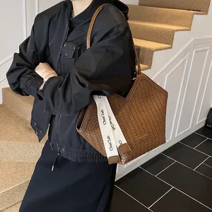 Détail d'un sac cabas marron tissé avec bandoulière à lettres et patch logo carré