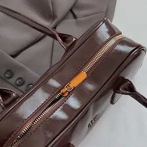 Detail der dunkelbraunen Lackledertasche mit goldenem Reißverschluss und Metall-Logo