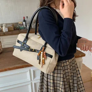 Detail view of beige canvas Boston bag with black leather straps and wooden bead charm
