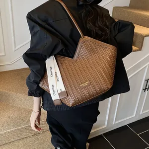 Détail du sac cabas tressé marron avec large bandoulière en tissu et logo doré