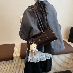 Detail der dunkelbraunen Boston-Tasche aus Lackleder mit Bärenanhänger und Riemen