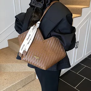 Détail d'un grand sac cabas tressé marron avec un foulard décoratif en soie sur l'anse