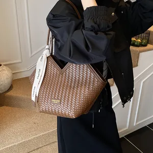 Gros plan sur un sac cabas tressé marron foncé avec foulard en soie et étiquette