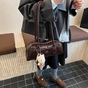 Detail einer dunkelbraunen Hochglanz-Zylindertasche mit Teddy-Anhänger und Metall-Logo