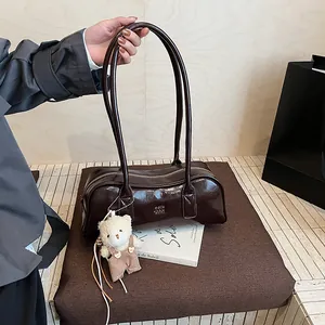 Nahaufnahme einer schokobraunen Lackledertasche mit süßem weißem Bärenanhänger