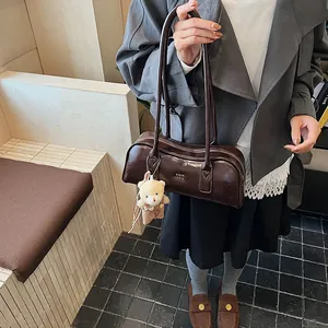 Detail der dunkelbraunen glänzenden Boston-Tasche mit Bärenanhänger und Retro-Gurt